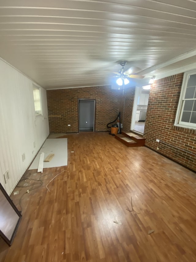 unfurnished living room with ceiling fan, lofted ceiling, brick wall, and wood-type flooring