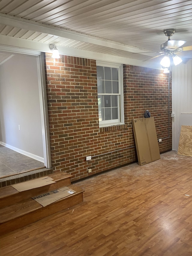 spare room with brick wall, beamed ceiling, wooden ceiling, ceiling fan, and hardwood / wood-style floors