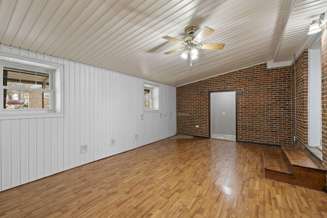 spare room with lofted ceiling, light hardwood / wood-style floors, ceiling fan, and brick wall