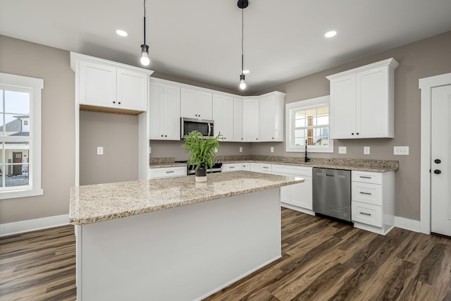 kitchen with white cabinetry, hanging light fixtures, appliances with stainless steel finishes, a kitchen island, and light stone countertops