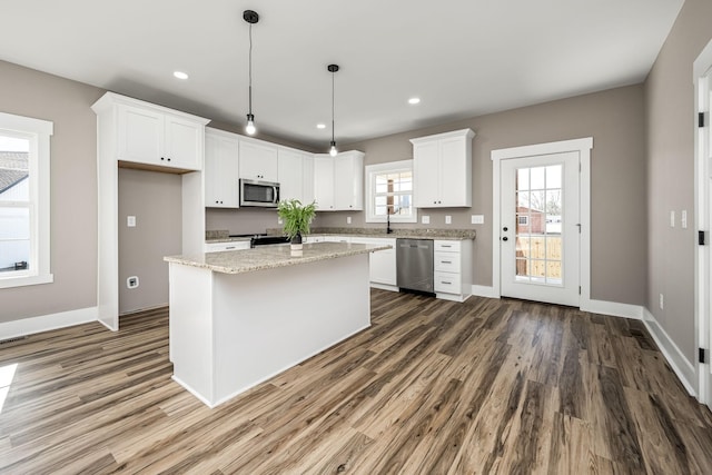 kitchen featuring pendant lighting, white cabinets, a center island, light stone counters, and stainless steel appliances