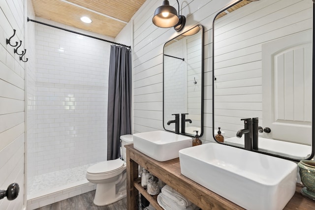 bathroom featuring toilet, hardwood / wood-style flooring, wood walls, vanity, and curtained shower