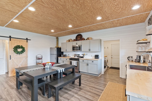 dining room featuring washer / clothes dryer, a barn door, light hardwood / wood-style flooring, wooden walls, and sink