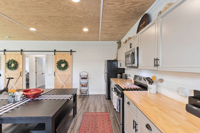 kitchen with a barn door, wood walls, dark hardwood / wood-style flooring, stainless steel appliances, and wooden counters