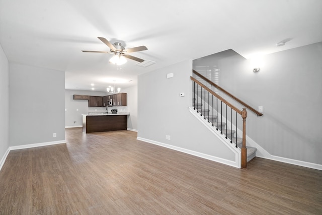 unfurnished living room featuring ceiling fan with notable chandelier and dark hardwood / wood-style floors