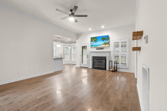 unfurnished living room featuring hardwood / wood-style flooring, ceiling fan with notable chandelier, crown molding, and a wealth of natural light