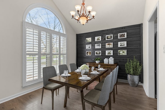 dining area with a chandelier, wood-type flooring, vaulted ceiling, and wood walls