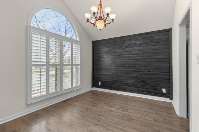 empty room featuring a chandelier, vaulted ceiling, and dark wood-type flooring