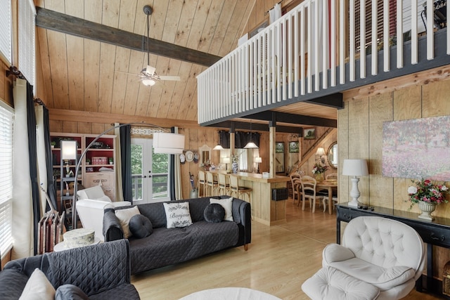 living room with ceiling fan, beamed ceiling, wooden walls, wooden ceiling, and light wood-type flooring