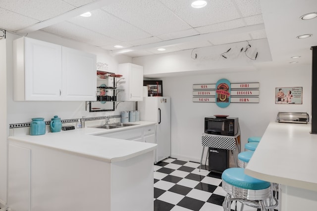 kitchen with white refrigerator, white cabinets, kitchen peninsula, a paneled ceiling, and sink