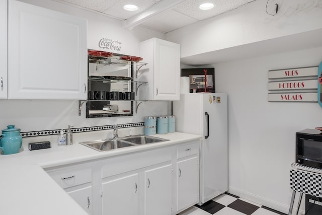 kitchen featuring a drop ceiling, sink, white fridge, and white cabinetry