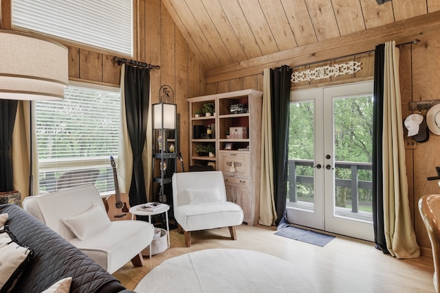 living area featuring a healthy amount of sunlight, lofted ceiling, wooden walls, and french doors