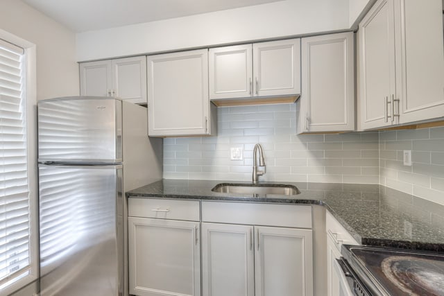 kitchen with dark stone counters, sink, tasteful backsplash, and stainless steel fridge