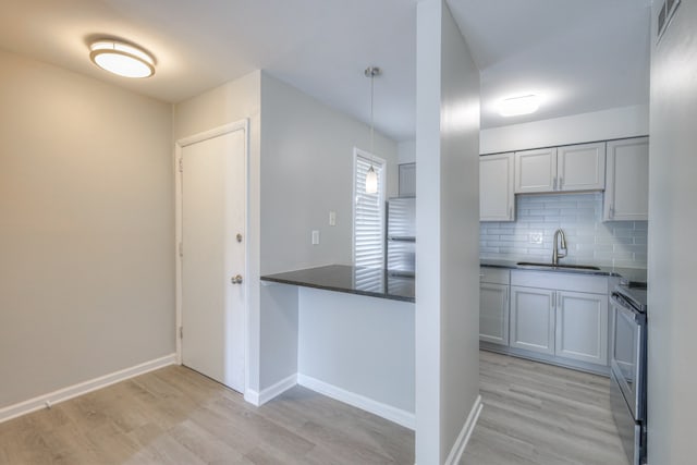 kitchen with tasteful backsplash, light hardwood / wood-style flooring, decorative light fixtures, sink, and electric range