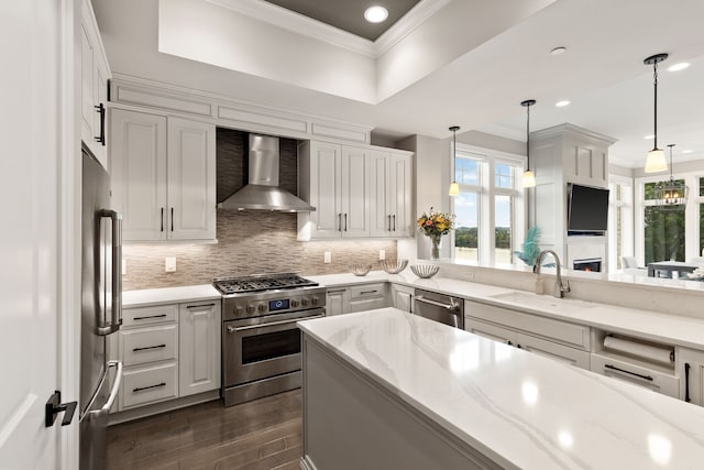 kitchen with stainless steel appliances, sink, decorative light fixtures, wall chimney exhaust hood, and light stone countertops