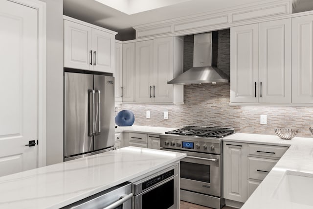 kitchen with tasteful backsplash, white cabinets, wall chimney exhaust hood, and high quality appliances