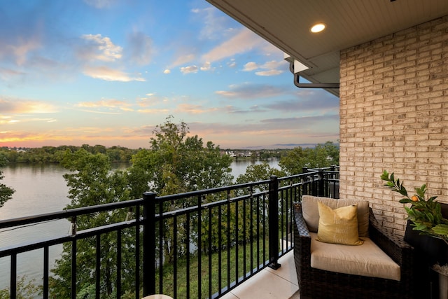 balcony at dusk featuring a water view