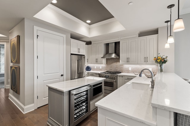 kitchen with wall chimney exhaust hood, premium appliances, stacked washer and dryer, beverage cooler, and a tray ceiling