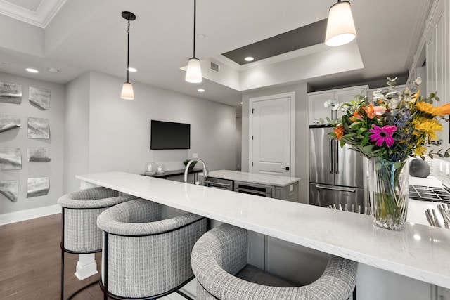 kitchen with hanging light fixtures, crown molding, light stone countertops, stainless steel fridge, and dark wood-type flooring