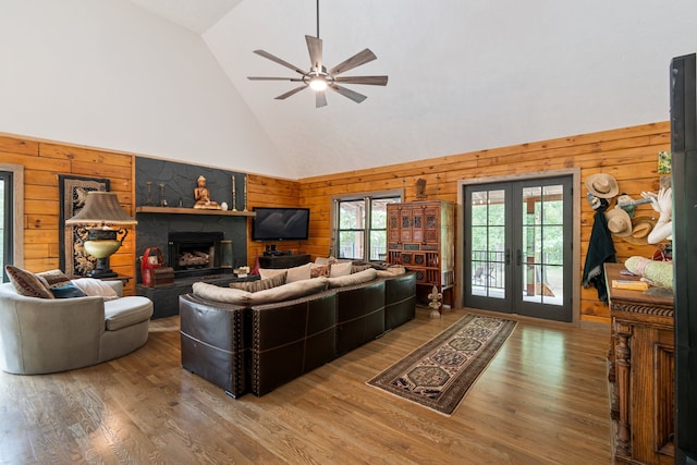 living room featuring wood-type flooring, a large fireplace, ceiling fan, french doors, and wooden walls