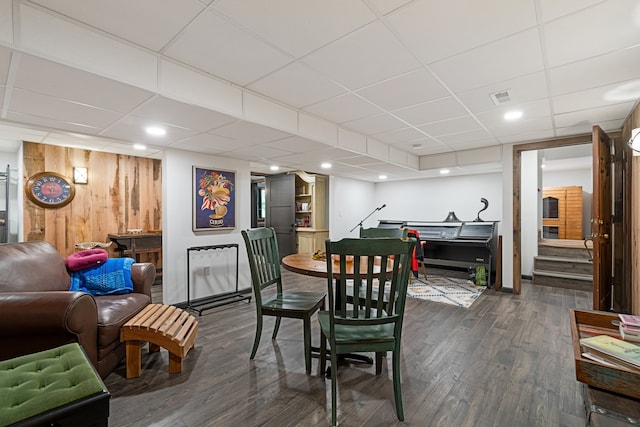 dining room featuring wooden walls, a drop ceiling, and dark wood-type flooring