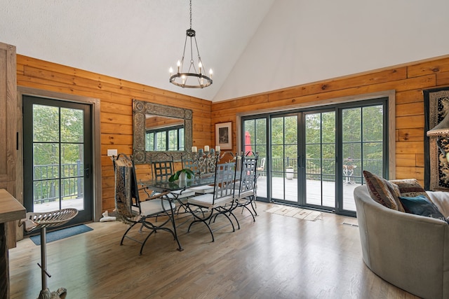 dining space featuring an inviting chandelier, hardwood / wood-style flooring, wooden walls, and high vaulted ceiling