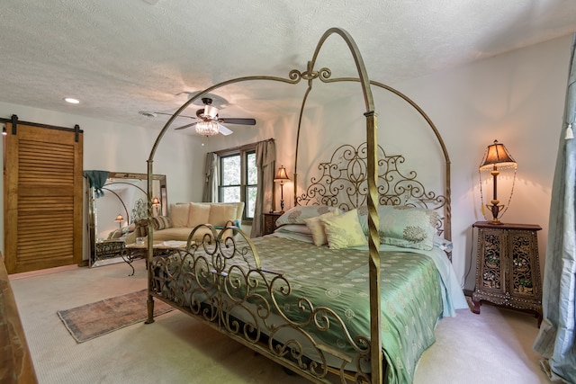 bedroom featuring light carpet, a textured ceiling, ceiling fan, and a barn door