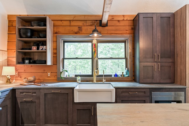 kitchen featuring a textured ceiling, dark brown cabinetry, wooden walls, and sink