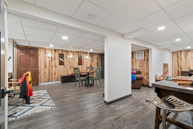 rec room with a drop ceiling, wooden walls, and dark hardwood / wood-style flooring