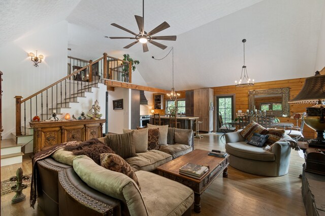 living room featuring a textured ceiling, dark hardwood / wood-style floors, ceiling fan with notable chandelier, wood walls, and high vaulted ceiling