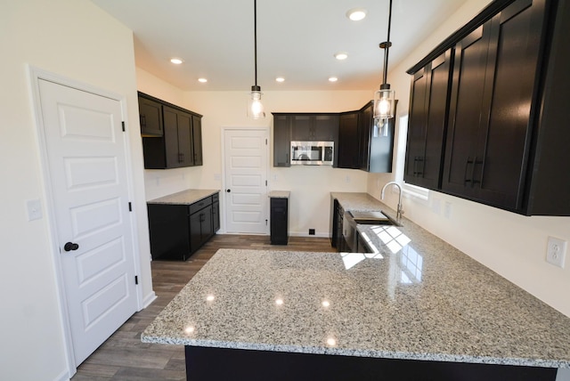 kitchen featuring dark wood-style floors, recessed lighting, stainless steel microwave, a sink, and light stone countertops