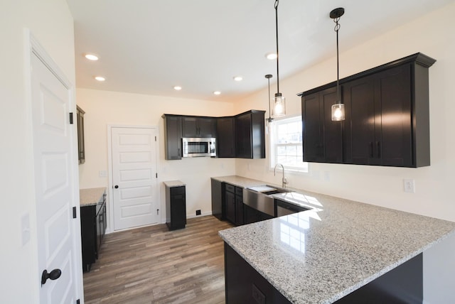 kitchen with light stone counters, a peninsula, a sink, hanging light fixtures, and stainless steel microwave