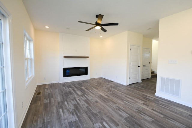 unfurnished living room with dark wood-style flooring, visible vents, stairway, a glass covered fireplace, and baseboards