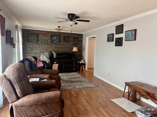 living room with wood-type flooring, a textured ceiling, wooden walls, crown molding, and ceiling fan