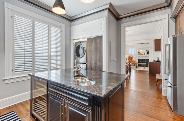 kitchen featuring stacked washer / drying machine, stainless steel refrigerator, a center island with sink, and plenty of natural light