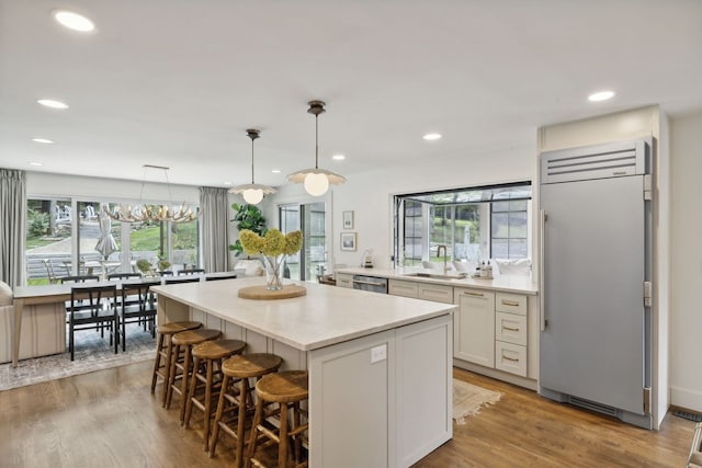 kitchen with pendant lighting, light wood-type flooring, sink, white cabinets, and built in fridge