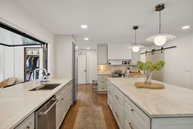 kitchen with dark wood-type flooring, a barn door, stainless steel appliances, decorative light fixtures, and sink