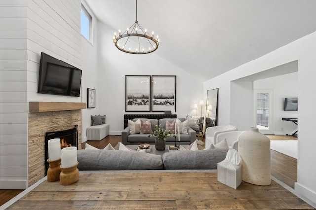 living room featuring high vaulted ceiling, a chandelier, hardwood / wood-style floors, and a stone fireplace