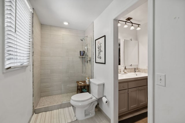 bathroom with a tile shower, vanity, and toilet