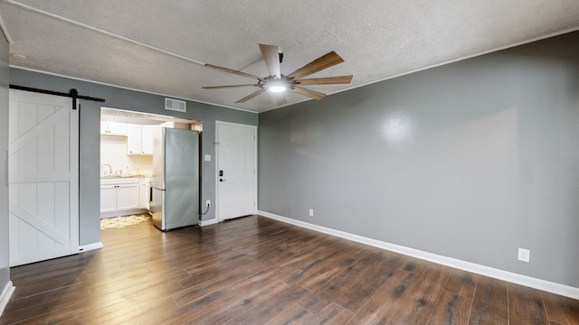 unfurnished bedroom featuring ceiling fan, dark wood-type flooring, stainless steel refrigerator, ensuite bath, and a barn door