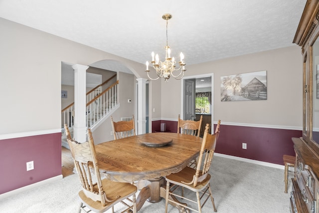 carpeted dining space featuring a notable chandelier, a textured ceiling, and ornate columns