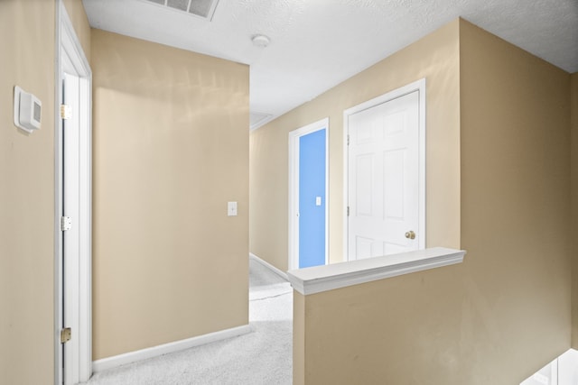 hallway with light colored carpet and a textured ceiling