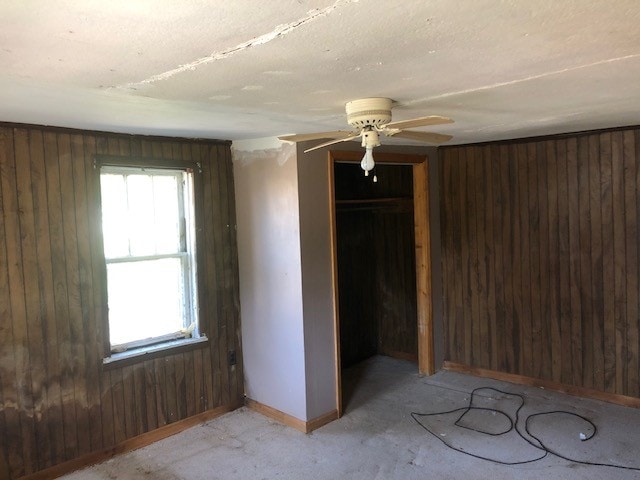 unfurnished bedroom with a closet, wooden walls, and ceiling fan