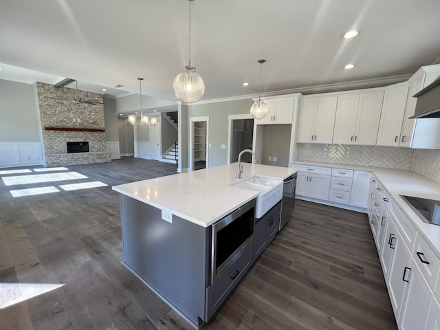 kitchen featuring a kitchen island with sink, white cabinets, a fireplace, and dark hardwood / wood-style flooring