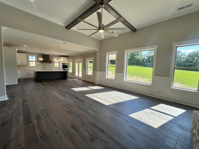 unfurnished living room featuring ceiling fan with notable chandelier, sink, dark wood-type flooring, and crown molding