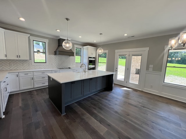 kitchen featuring an island with sink, white cabinets, dark wood-type flooring, and premium range hood