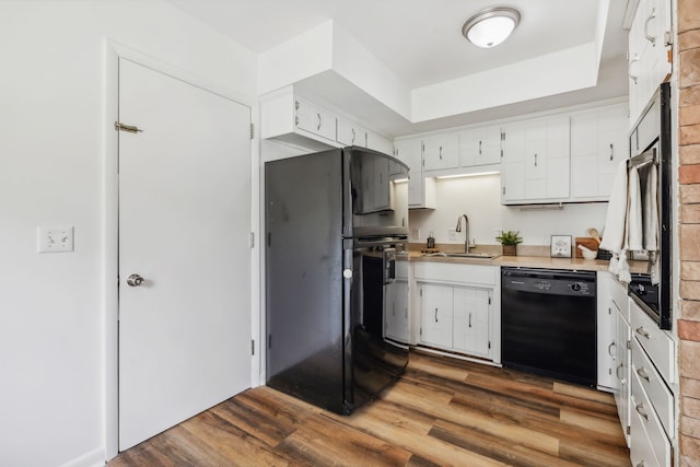 kitchen with a tray ceiling, dark hardwood / wood-style floors, sink, white cabinetry, and black appliances