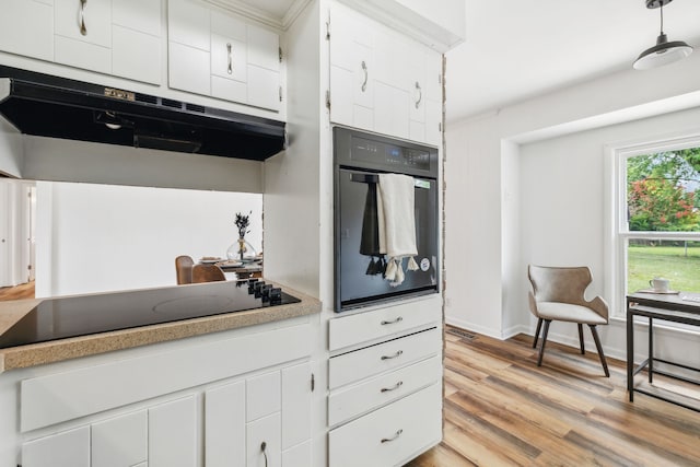 kitchen featuring light wood-type flooring, white cabinets, hanging light fixtures, black appliances, and crown molding