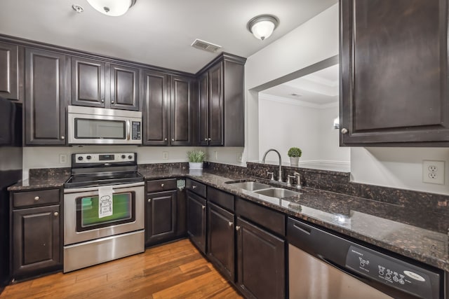 kitchen with appliances with stainless steel finishes, dark brown cabinets, dark stone counters, dark hardwood / wood-style floors, and sink