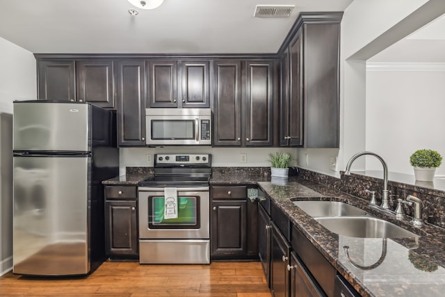 kitchen featuring sink, stainless steel appliances, dark stone countertops, crown molding, and light hardwood / wood-style floors